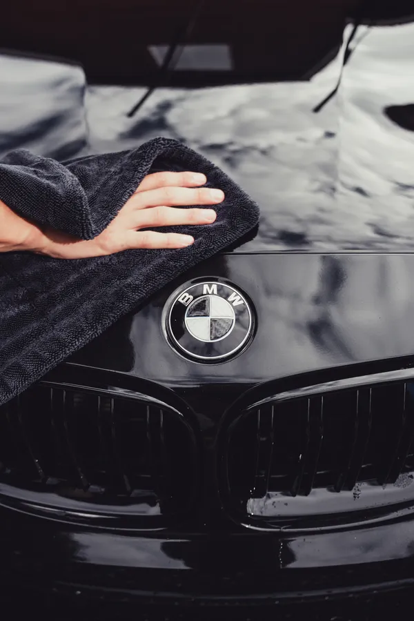 Towel wiping the glossy black hood of a BMW after a detail